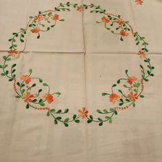 an embroidered tablecloth with orange flowers and green leaves on white linen, laid out in a circle