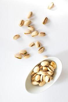 pistachio nuts in a white bowl on a white surface with scattered pieces of pistachio