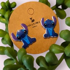 two blue and purple earrings sitting next to each other on top of green leaves in front of a white background