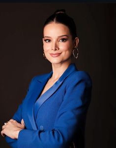 a woman with her arms crossed and wearing a blue blazer, standing in front of a black background