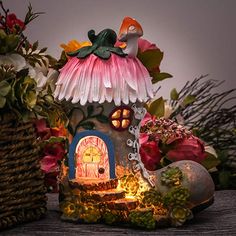 a fairy house with flowers and plants around it on a table next to a wicker basket