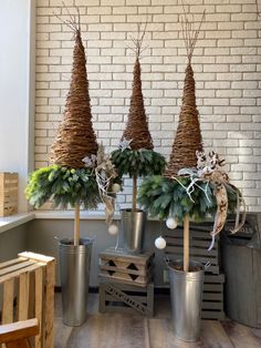 three metal buckets filled with christmas trees and greenery in front of a brick wall