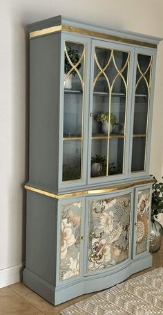 an old china cabinet painted in blue and gold with flowers on the front, along with a potted plant