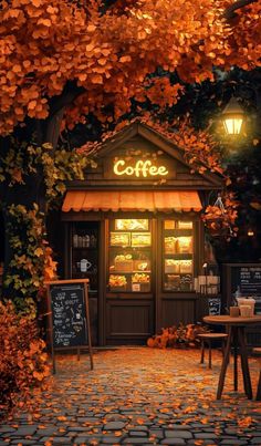 an autumn scene with leaves on the ground and a coffee shop in the background at night