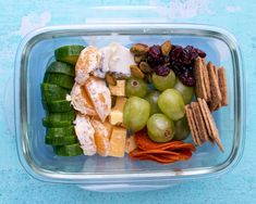 a plastic container filled with grapes, crackers, nuts and other food on top of a blue surface