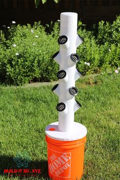 an orange bucket sitting in the grass next to a white pole with buttons on it