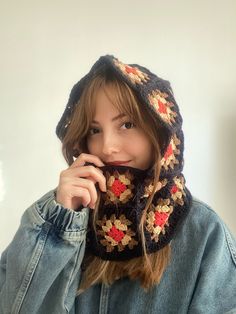 a young woman wearing a knitted hat and scarf with red flowers on the hood