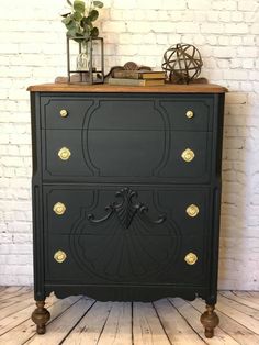 an old dresser painted black and gold with brass knobs on the front, sitting against a white brick wall