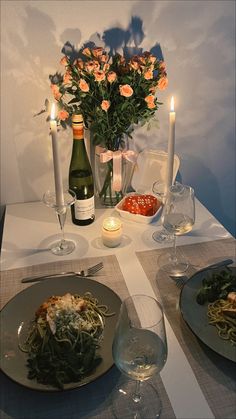 the table is set with wine, pasta and flowers in vases next to candles