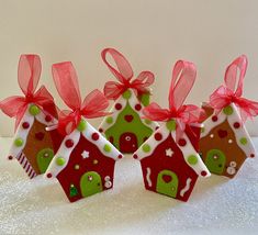 three small gingerbread houses decorated with red bows and green decorations on top of a white table