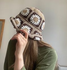 a woman wearing a brown and white crochet hat while holding her hand up to her face