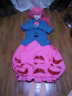 a doll is laying on the floor in a pink dress and blue jacket with red letters