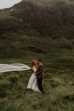 a bride and groom standing in the grass with their veil blowing in front of them