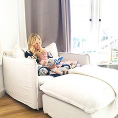 a woman sitting on top of a white couch next to a baby in a bed