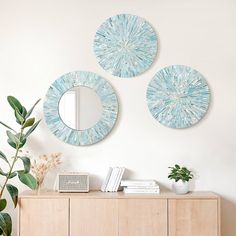 three circular mirrors mounted on the wall above a wooden sideboard with books and plants