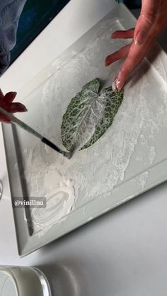 a person is painting a leaf on a white tray with flowers and leaves around it