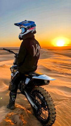 a man riding on the back of a dirt bike in the middle of desert at sunset