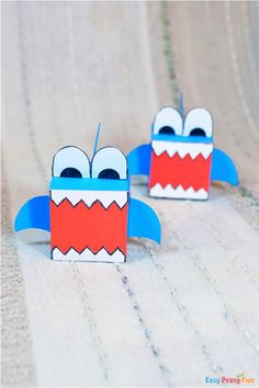 two paper monsters sitting on top of a table next to each other with eyes and mouths