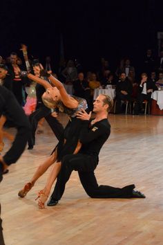 two people are dancing on the dance floor with their arms around each other while others watch