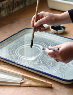 a person is holding a pencil and drawing on a glass tray with paintbrushes