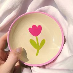 a hand holding a pink and green bowl with a flower painted on it's side