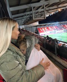 a woman holding a small child in her arms at a soccer game while sitting on the bleachers