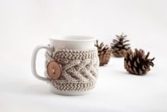 a coffee cup with a button on it next to some pine cones