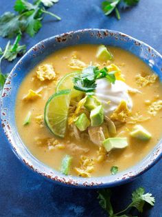 a blue bowl filled with soup and topped with sour cream, avocado and cilantro