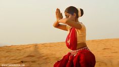 a woman standing in the sand with her hands up to her face and wearing a red sari