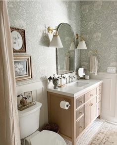 a white toilet sitting next to a bathroom sink under a mirror and two lamps on top of it