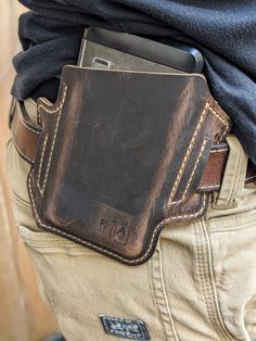 a close up of a person holding a cell phone in their back pocket and wearing a leather belt