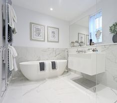 a white bathroom with marble flooring and large bathtub in the center, along with two framed pictures on the wall