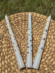 two white candles sitting on top of a woven basket next to each other in the grass