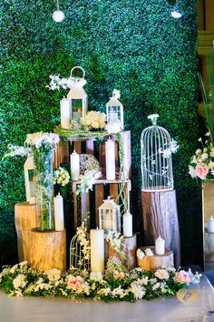 an arrangement of candles, flowers and birdcages is displayed in front of a green wall