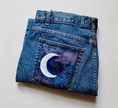 a pair of blue jeans with the moon painted on it's back pocket, sitting on a white surface