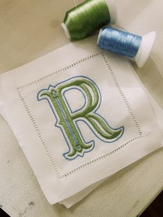 two spools of thread sit next to a monogrammed napkin with the letter r on it