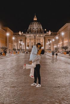 a man and woman standing in front of a building at night with the lights on