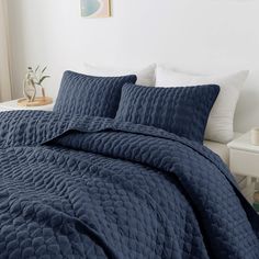 a bed with blue comforter and pillows in a room next to a white table