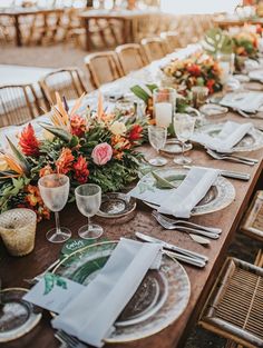 a long table set with place settings and flowers on it for an outdoor dinner party