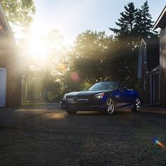 a blue car parked in front of a barn with the sun shining down on it