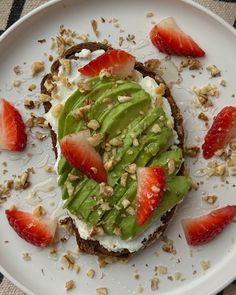 a white plate topped with an open face sandwich covered in avocado and strawberries