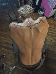 a man sitting on the floor with his back turned to the camera and tattoos on his chest