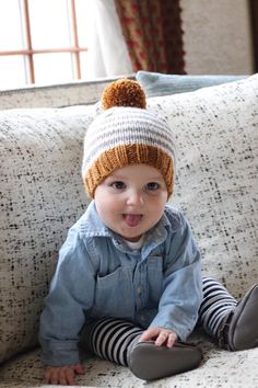 a little boy sitting on top of a couch wearing a knitted hat and striped pants