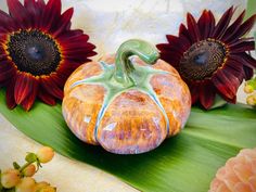 an orange pumpkin sitting on top of a green leaf next to red and yellow flowers