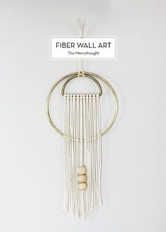 a white and gold wall hanging with two wooden beads on it's end, next to a sign that says fiber wall art