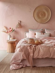 a bed with pink sheets and pillows in a room next to a basket on the wall