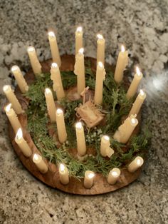 a bunch of lit candles sitting on top of a wooden plate covered in greenery