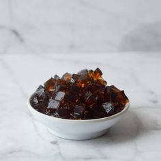 a white bowl filled with brown sugar cubes on top of a marble countertop