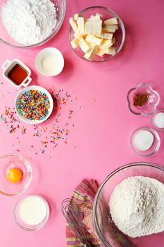 ingredients to make cake sitting on a pink surface with sprinkles and eggs