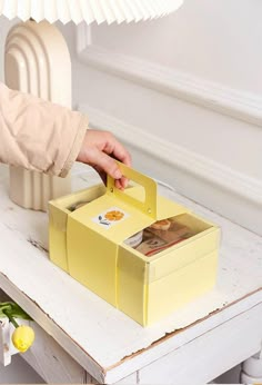 a person holding a card in a yellow box on top of a table next to a lamp